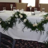 White banquet table with green floral garland and glassware in a decorated dining room
