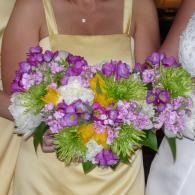 Person holding a bouquet of purple, white, and yellow flowers against a beige dress