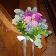 Bouquet of pink, purple, and white flowers tied with a white ribbon on a wooden pew