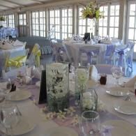 Elegant banquet room with white table settings, floral centerpieces, and large windows along the wall