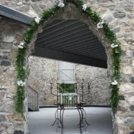 Stone archway with greenery framing a courtyard table and chairs in a rustic passageway