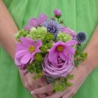 Hands holding a small bouquet of pink and purple flowers against a green dress