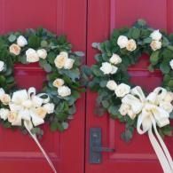 Two white floral wreaths with bows hanging on red double doors