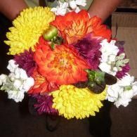 A hand-held bouquet of colorful flowers, including yellow, orange, purple, and white blooms.