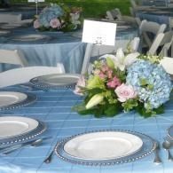 Blue banquet table with white plates and pastel flower centerpieces, set for an event
