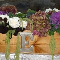 Floral arrangement in a wooden box with a silver letter E on a table
