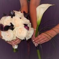 Two bridal bouquets: white roses with dark accents and a white calla lily, held by hands in purple dresses