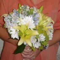 Person holding a bouquet of white and yellow flowers against a peach shirt