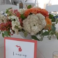 Flower centerpiece on a table with a red-bordered sign reading “Lansing”