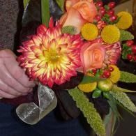 Handheld bouquet with pink, yellow, and orange flowers, green foliage, and silver ribbon accents