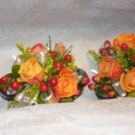 Two small floral arrangements with orange and yellow roses, berries, and greenery on a white surface