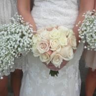 Bride holding a white rose bouquet with baby’s breath at a wedding, wearing a lace dress