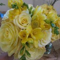 Yellow and white floral bouquet with roses, daisies, and greenery in a glass vase