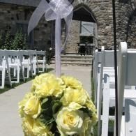 Yellow roses tied to a white chair in an outdoor wedding aisle with white chairs and a stone building backdrop