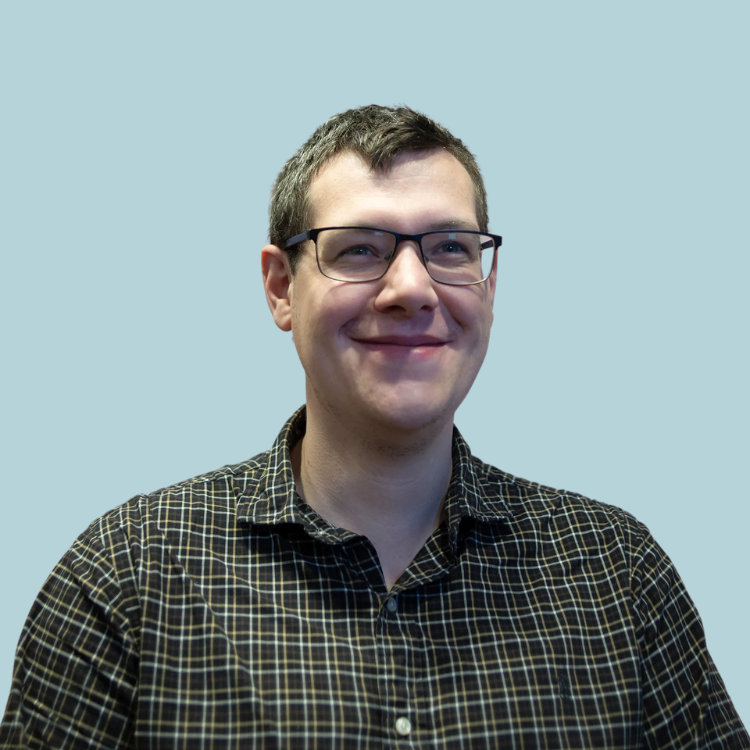 A man wearing glasses and a plaid shirt is smiling