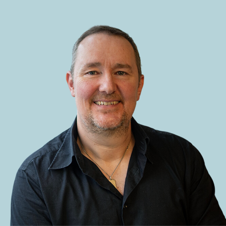 A man wearing a black shirt and a gold necklace is smiling for the camera.