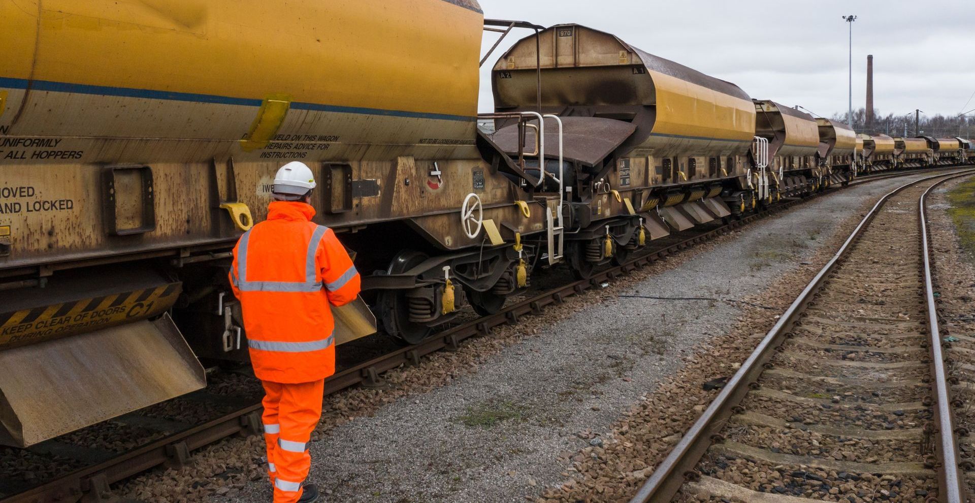 a person with orange jacket and orange pants between a train and rails