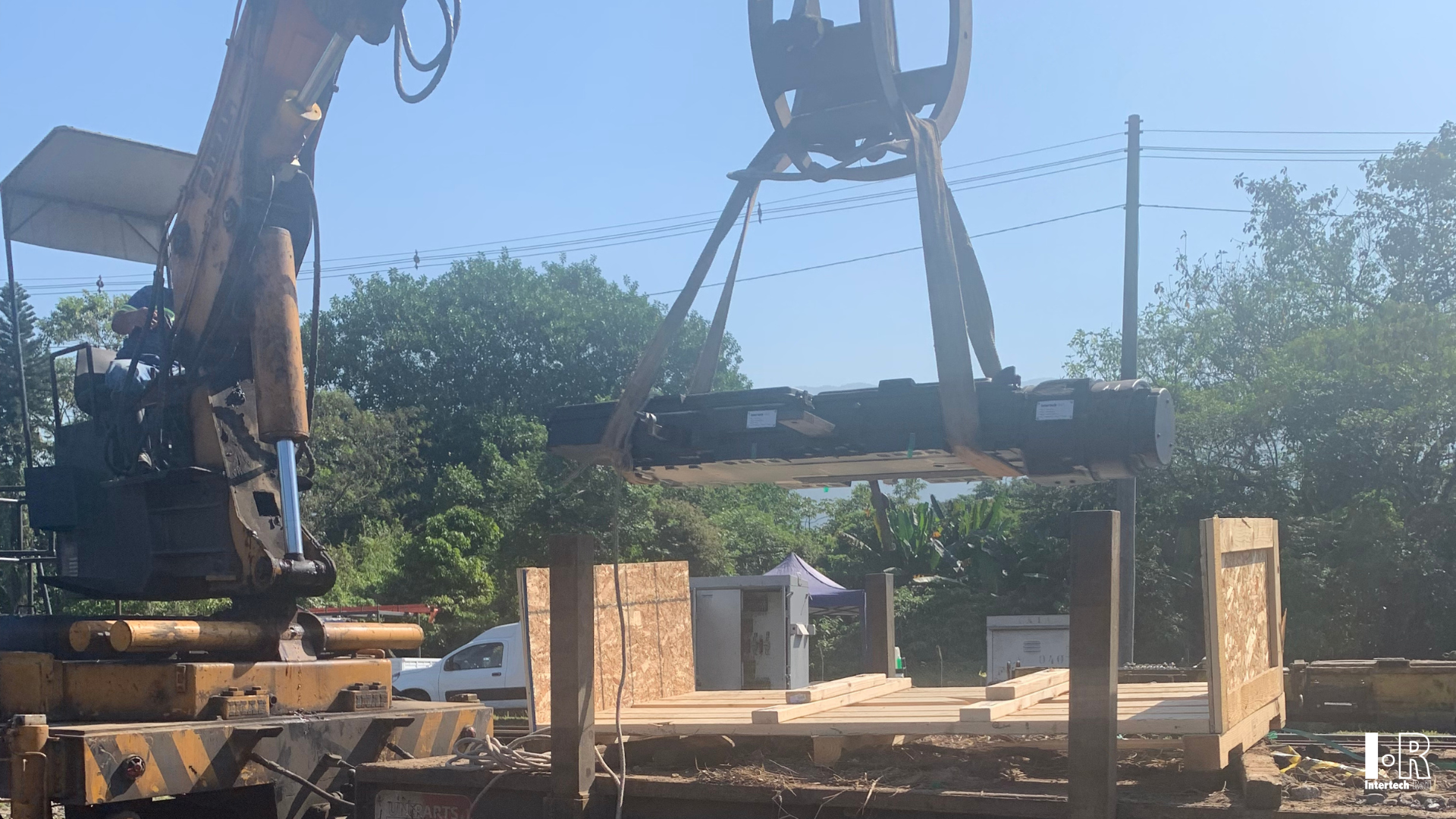 Rail construction site with an excavator lifting an IR5G switch machine by Intertech Rail over a partially built structure.
