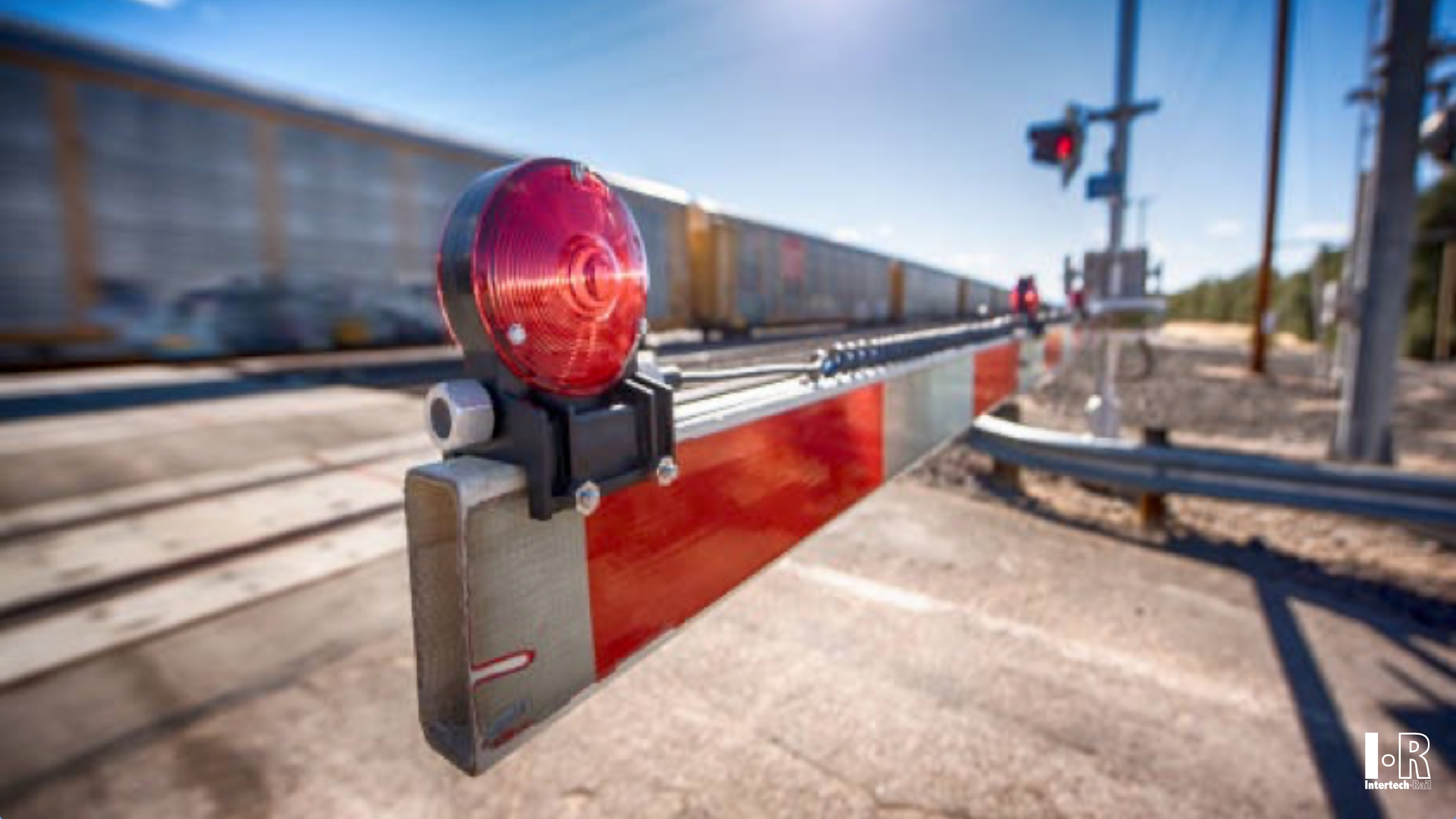 Railway crossing barrier with red warning light beside train tracks, blurred train passing in the background, Railway level crossing gate barrier - Intertech Rail
