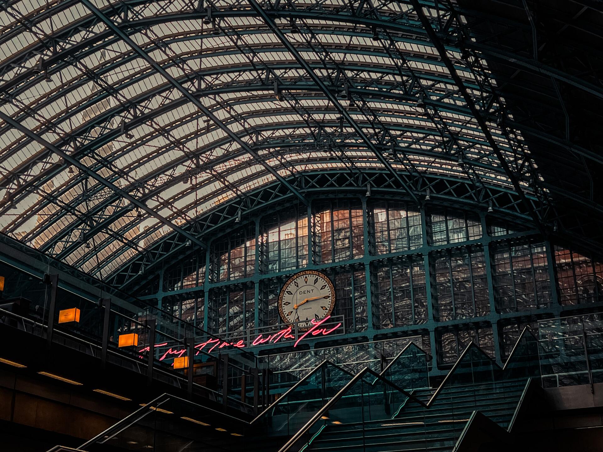 There is a clock on the ceiling of a train station.