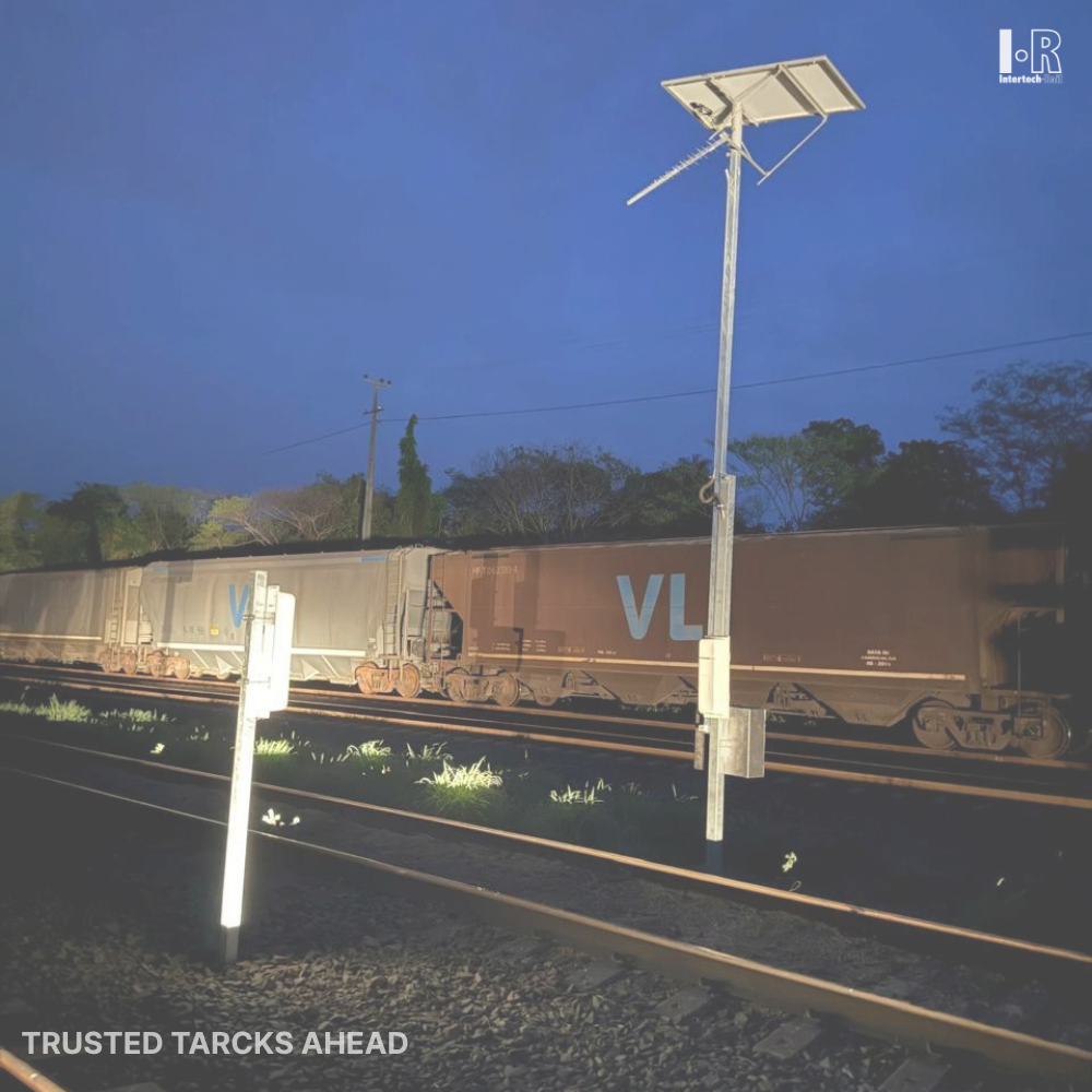 Freight train passing a dimly lit railway crossing at dusk under a blue sky