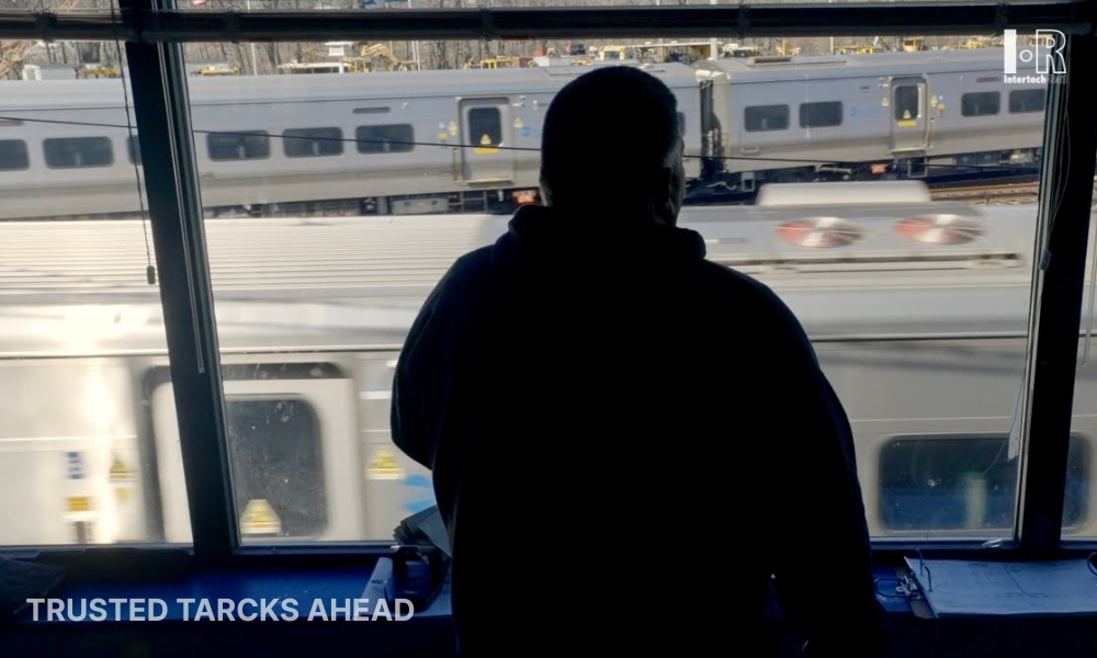 Silhouetted person looking out a window at passing train cars, with “TRUSTED TACKS AHEAD” text in the corner