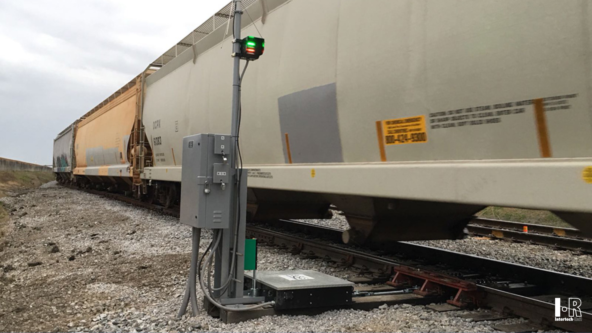 Freight train cars beside  an IRYM-16 hydraulic switch machine by Intertech Rail