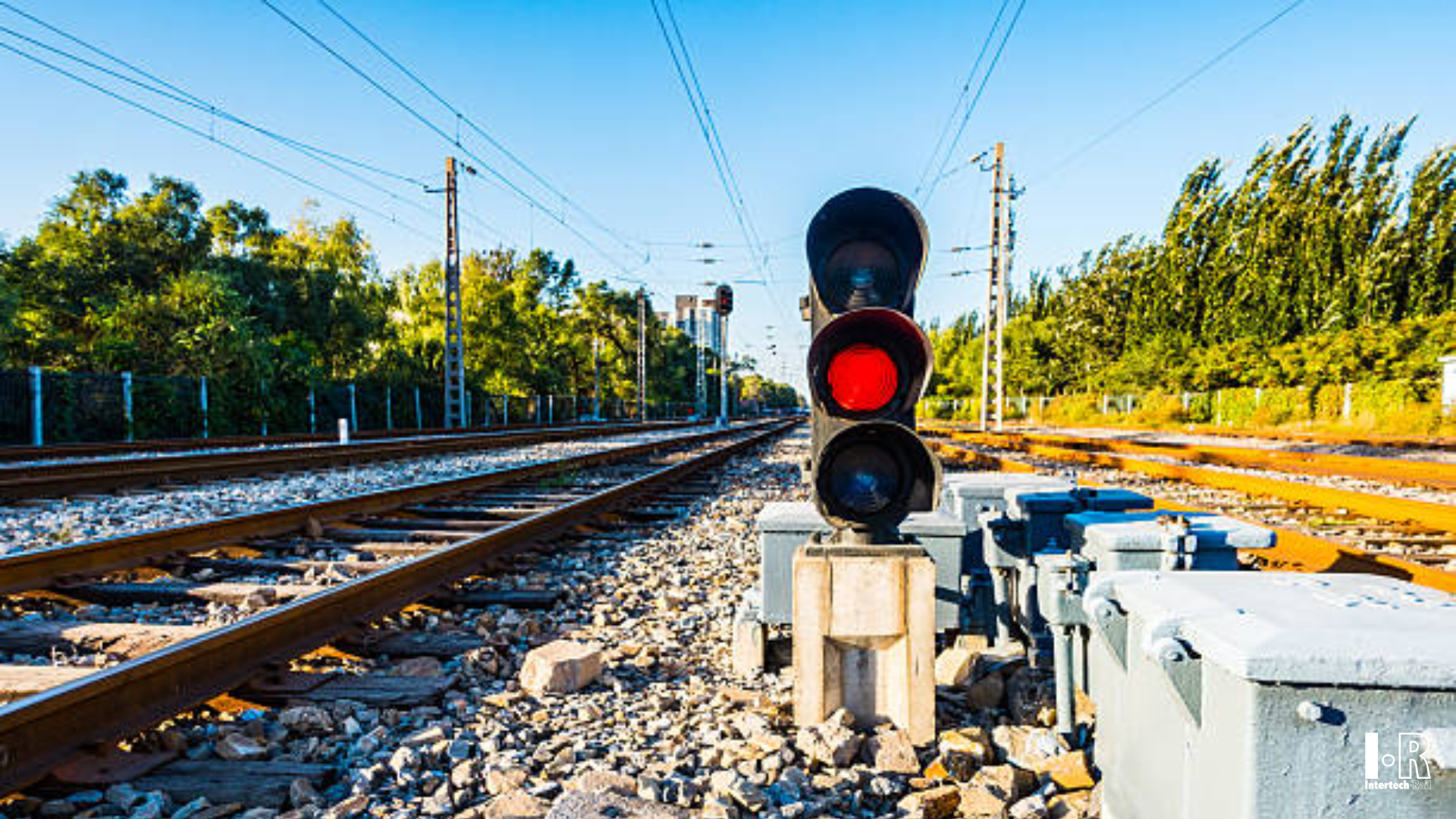 Red railway signal beside tracks under a clear blue sky, Three-light LED signal for railway level crossing - Intertech Rail