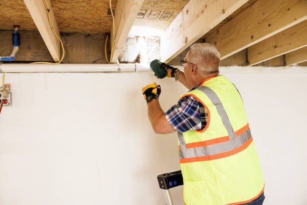 A man in a yellow vest is working on a wall with a drill.