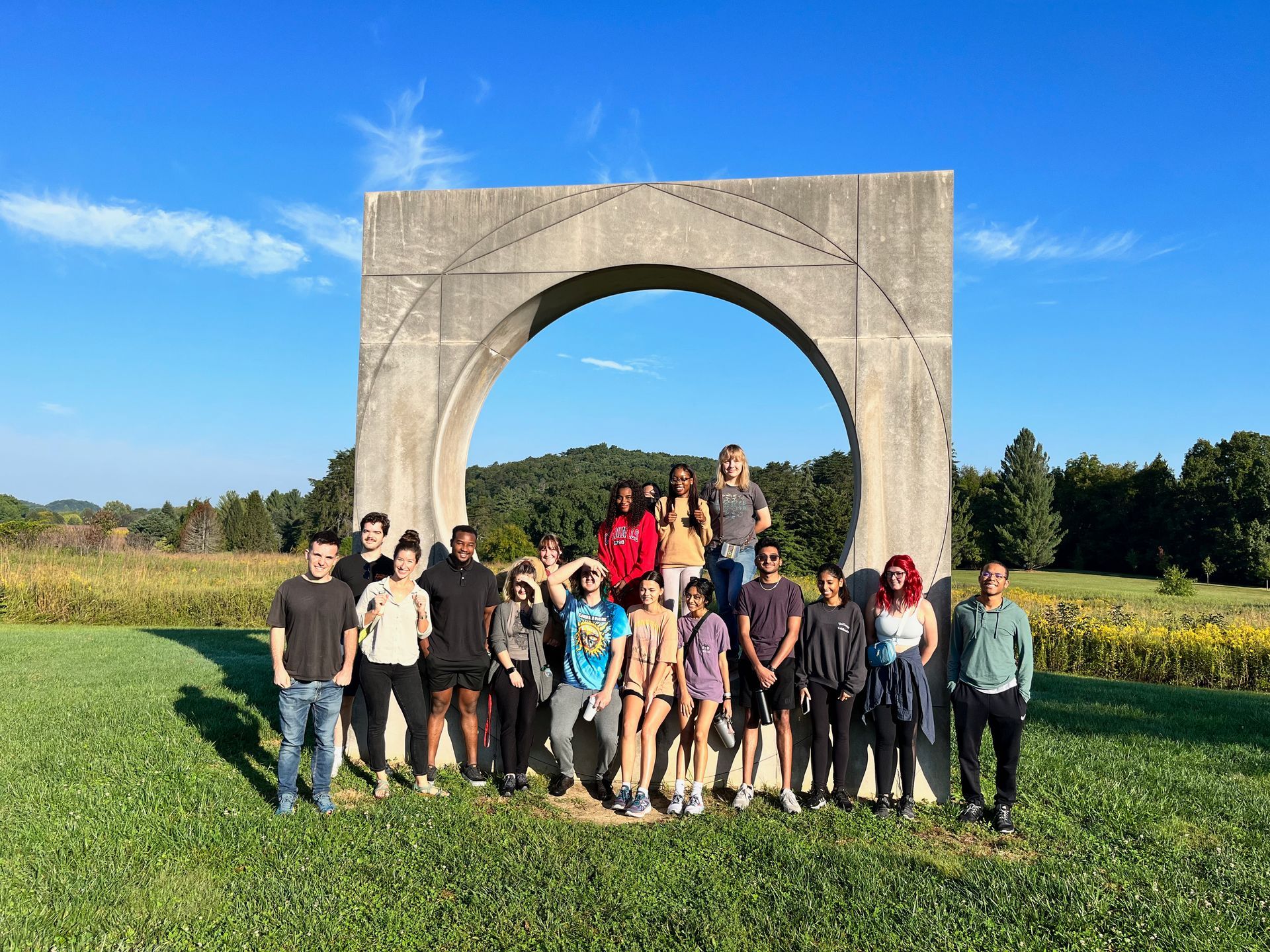 Group of students in front of a concrete circle art installation on a large, green prairie in Bernheim Forest