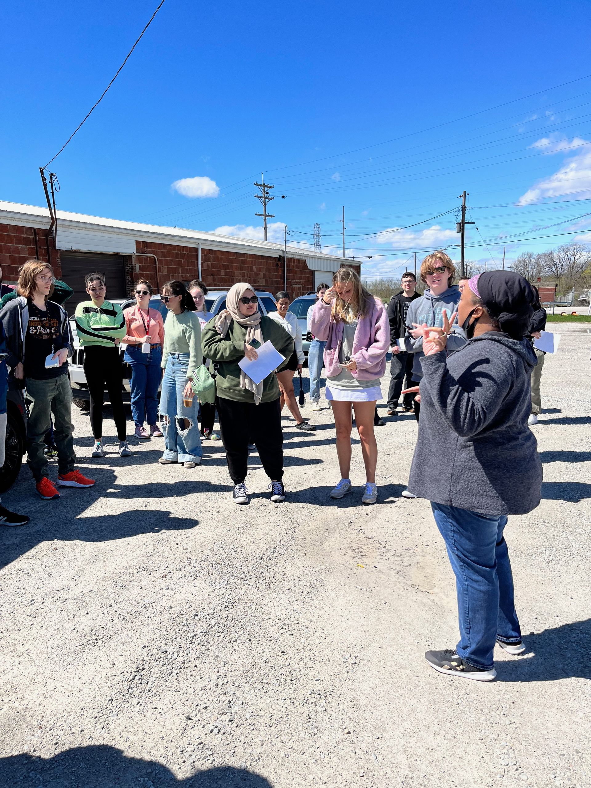 Students standing on a gravel road, listening to an environmental organizer talk about injustice 