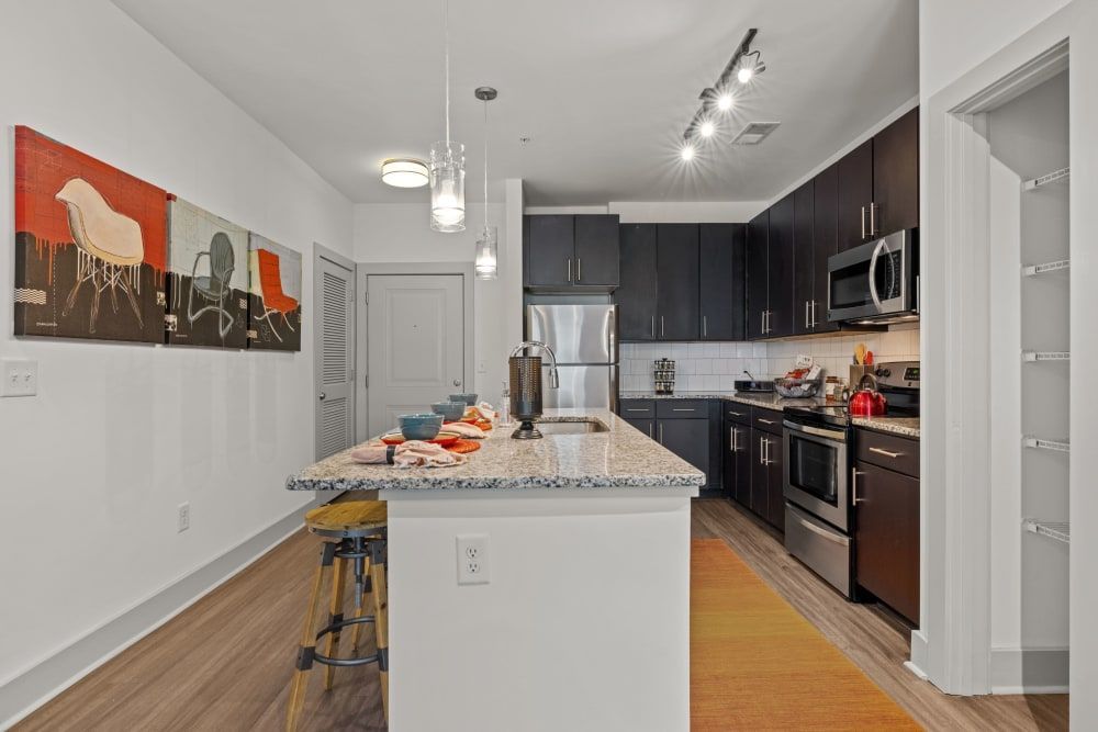 A side view of the apartment kitchen with a large island, designer lighting, and stainless steel appliances at Skyline West in Atlanta, GA.
