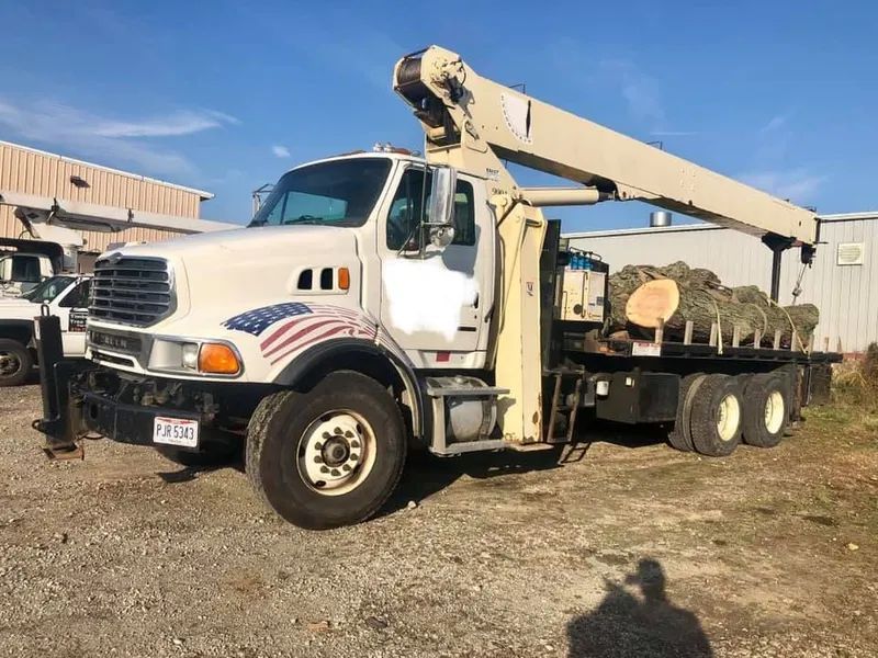 A white truck with a crane on the back is parked in a gravel lot.