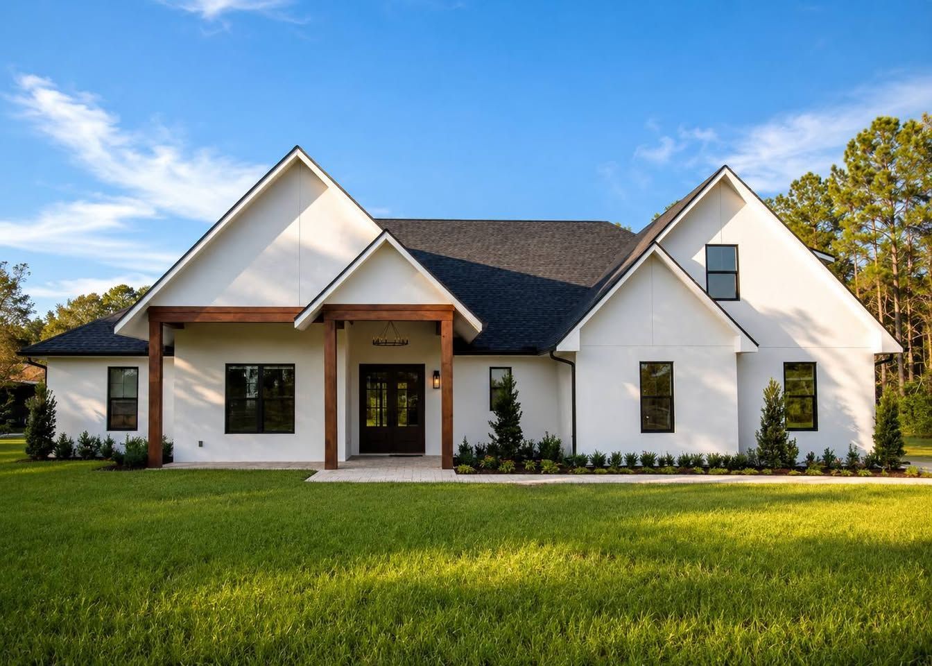 Modern white house with black roof, front porch, and green lawn under a blue sky