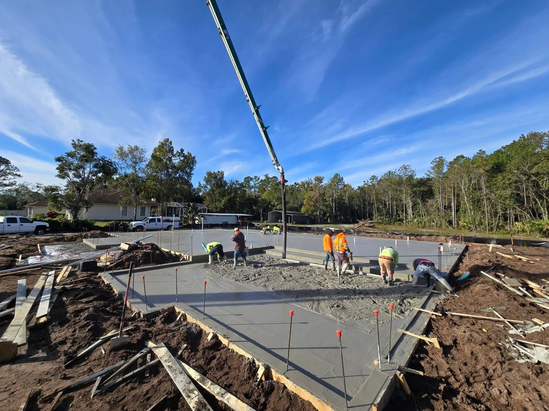 Concrete foundation under construction with workers, rebar, and a pump hose at an outdoor site