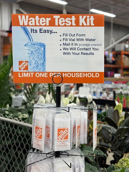 Store display sign for a free water test kit, orange and white, hanging above packaged kits in a garden center