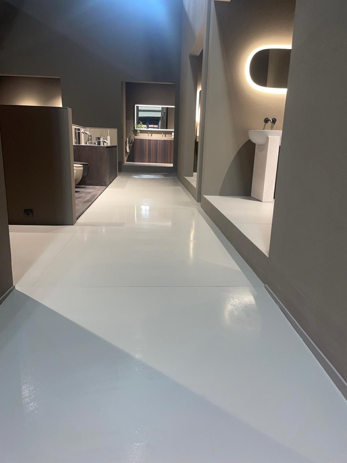 Corridoio moderno con pavimento bianco lucido, pareti grigie e illuminazione a incasso calda, che conduce a una zona trucco.