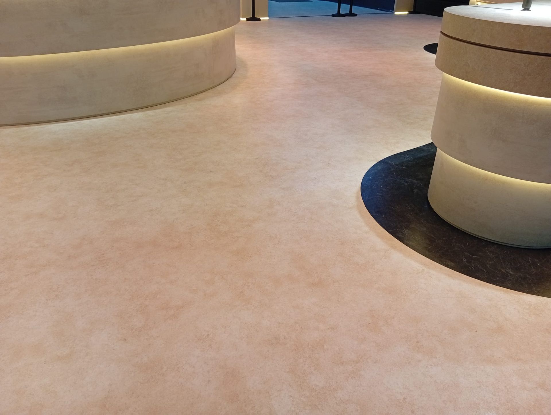 In un moderno spazio interno, un corridoio rivestito di moquette beige si snoda tra colonne curve color crema.