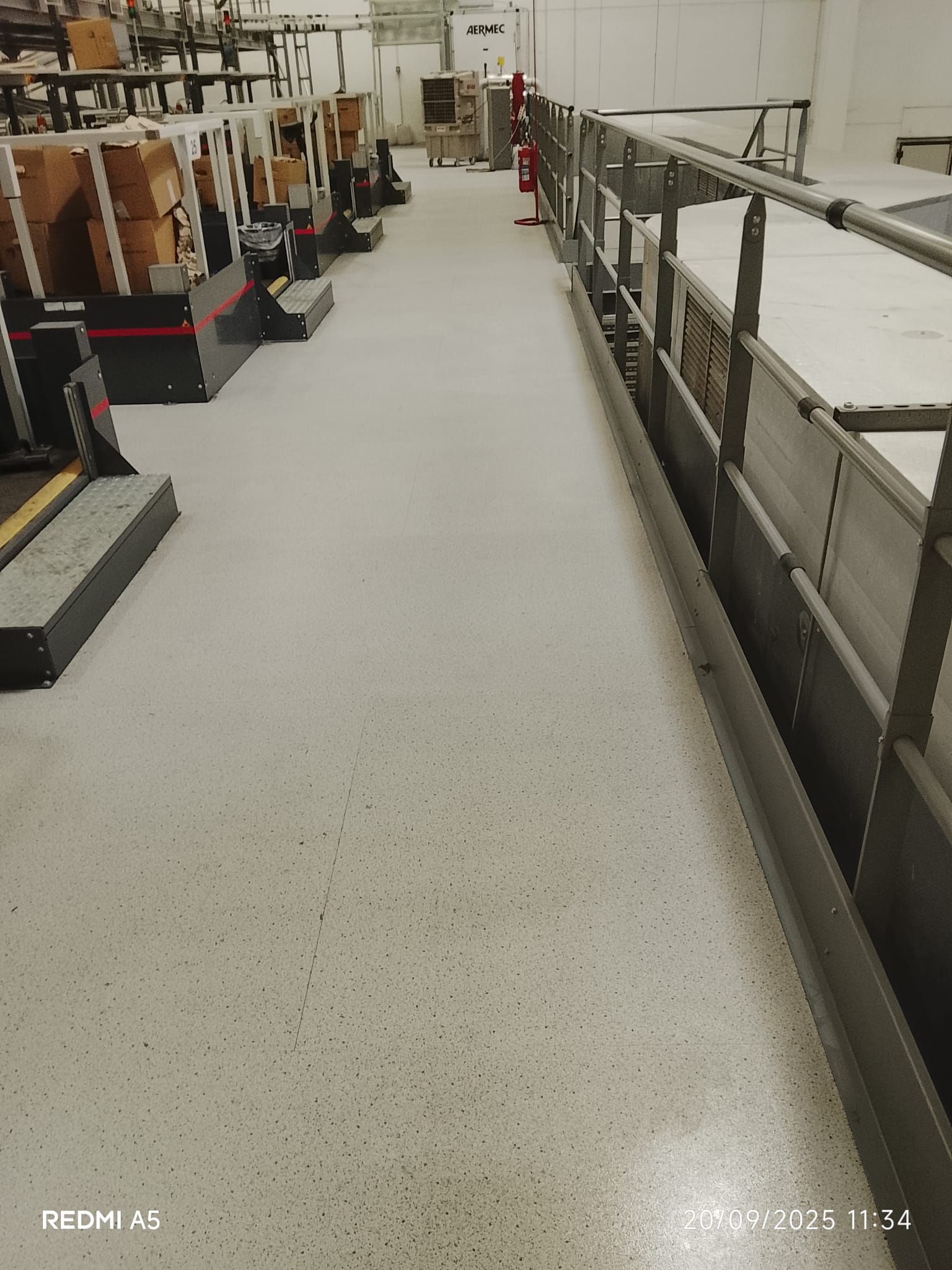 Passaggio industriale interno accanto a macchinari e ringhiere su un pavimento bianco