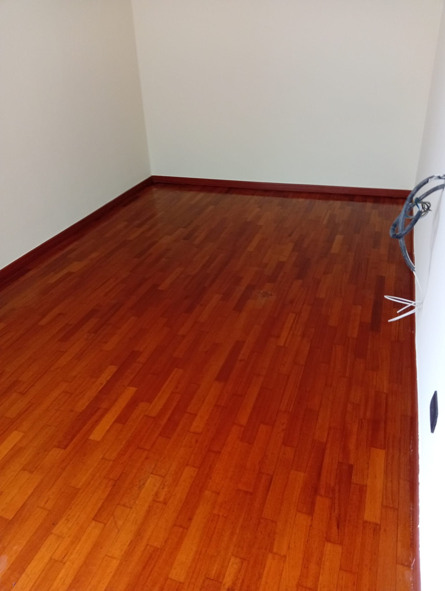 Stanza vuota con pareti bianche e pavimento in legno lucido color marrone rossastro.