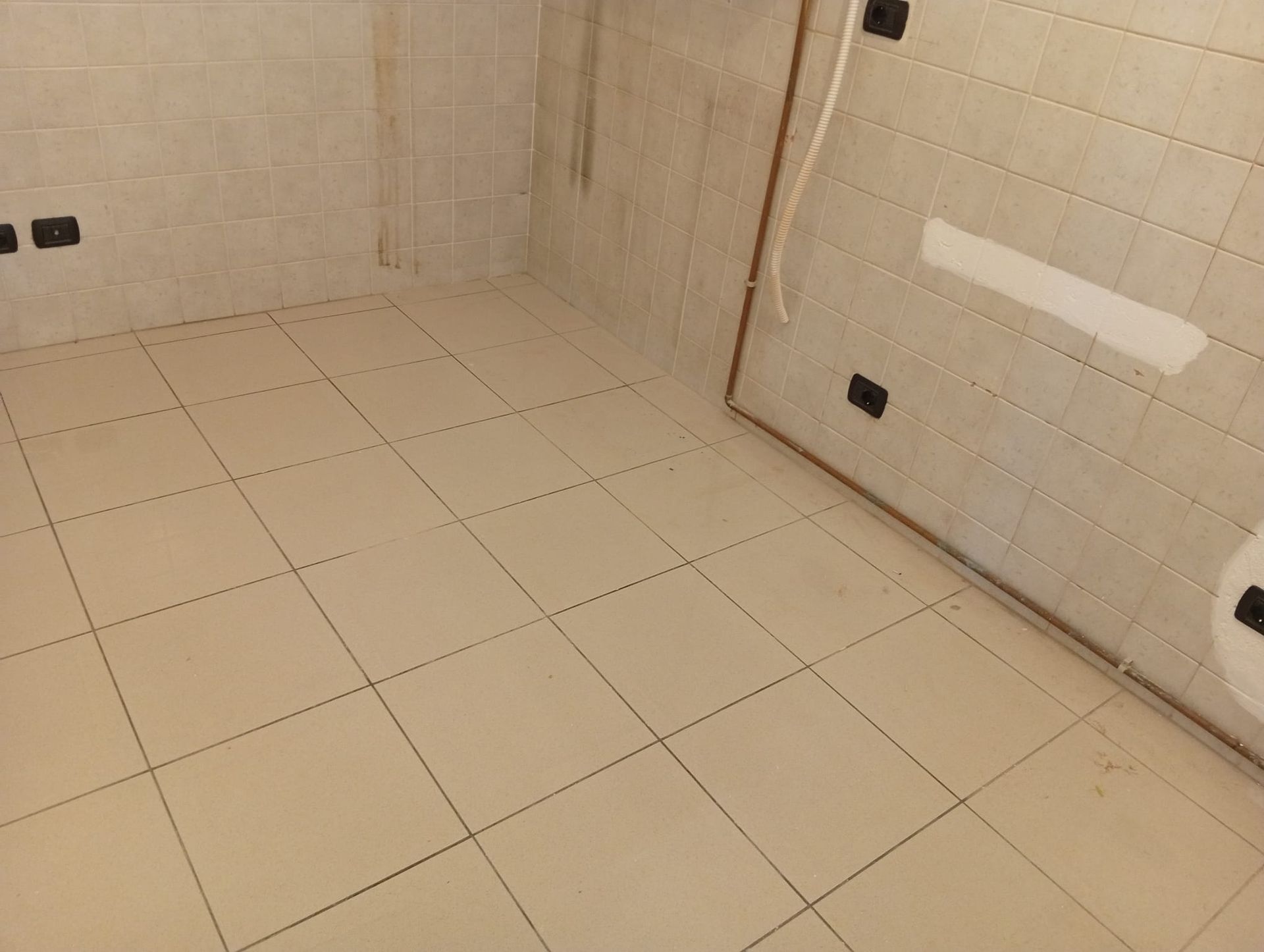 Stanza vuota con pareti e pavimento piastrellati di beige, probabilmente un bagno o un locale di servizio.