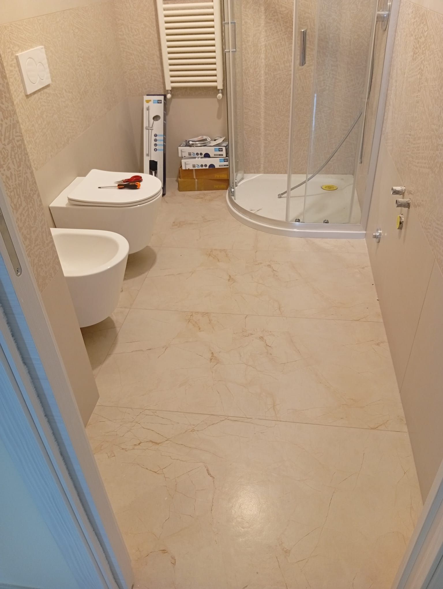Piccolo bagno beige con WC, box doccia e mobiletto lavabo bianco.