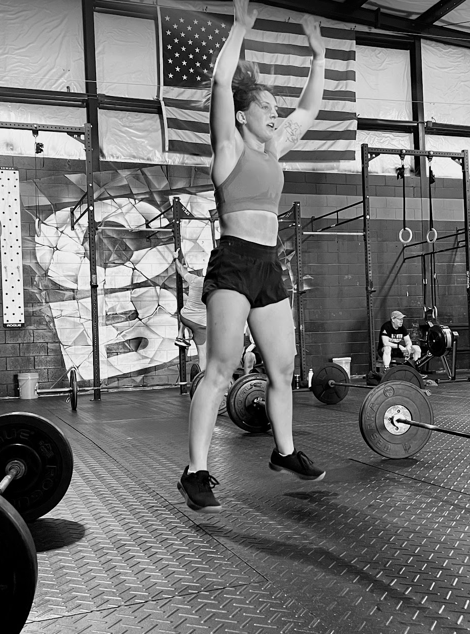 Athlete lifting a barbell overhead in a gym, with an American flag in the background.