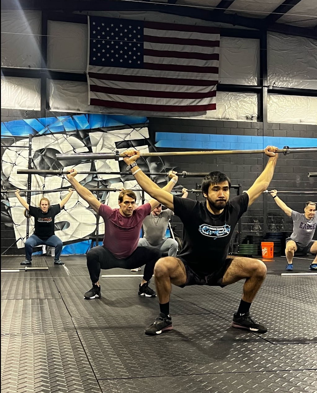 People doing overhead squats in a gym beneath an American flag