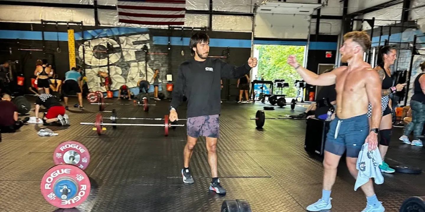 People in a gym lifting weights during a workout, with a coach pointing and bars on the floor.