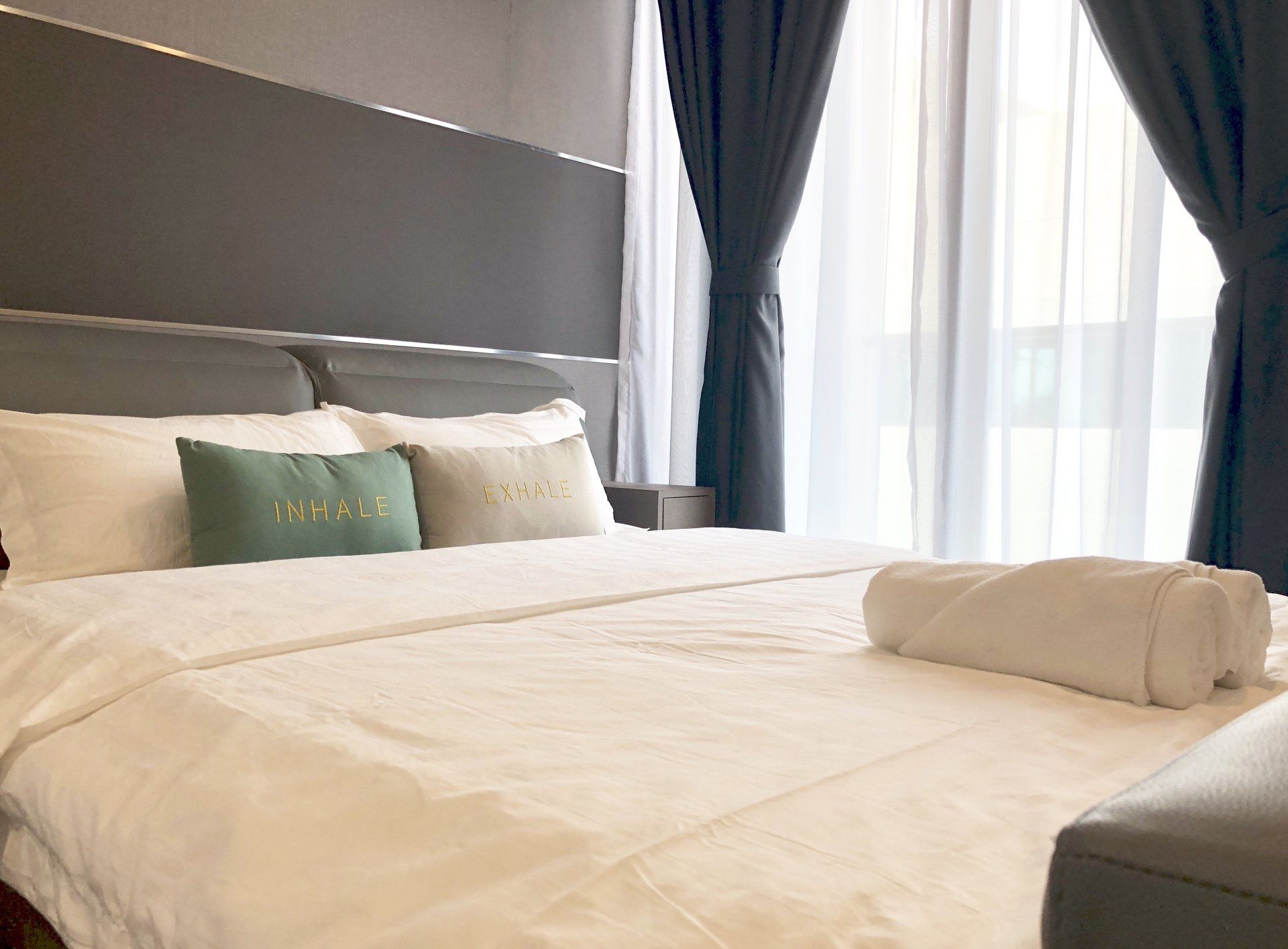 A bed with white sheets and pillows in a bedroom next to a window.