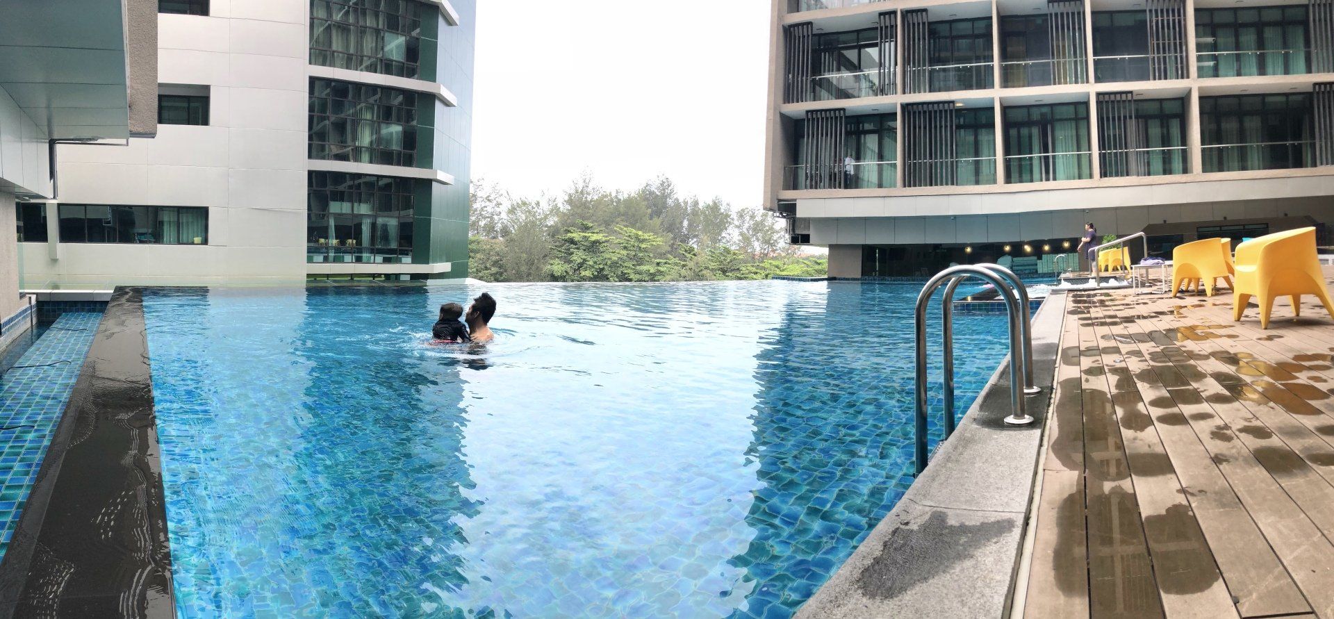 Two people are swimming in an infinity pool in front of a building.