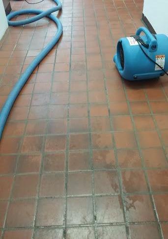 Un aspirateur bleu est posé sur un sol carrelé à côté d'un tuyau.