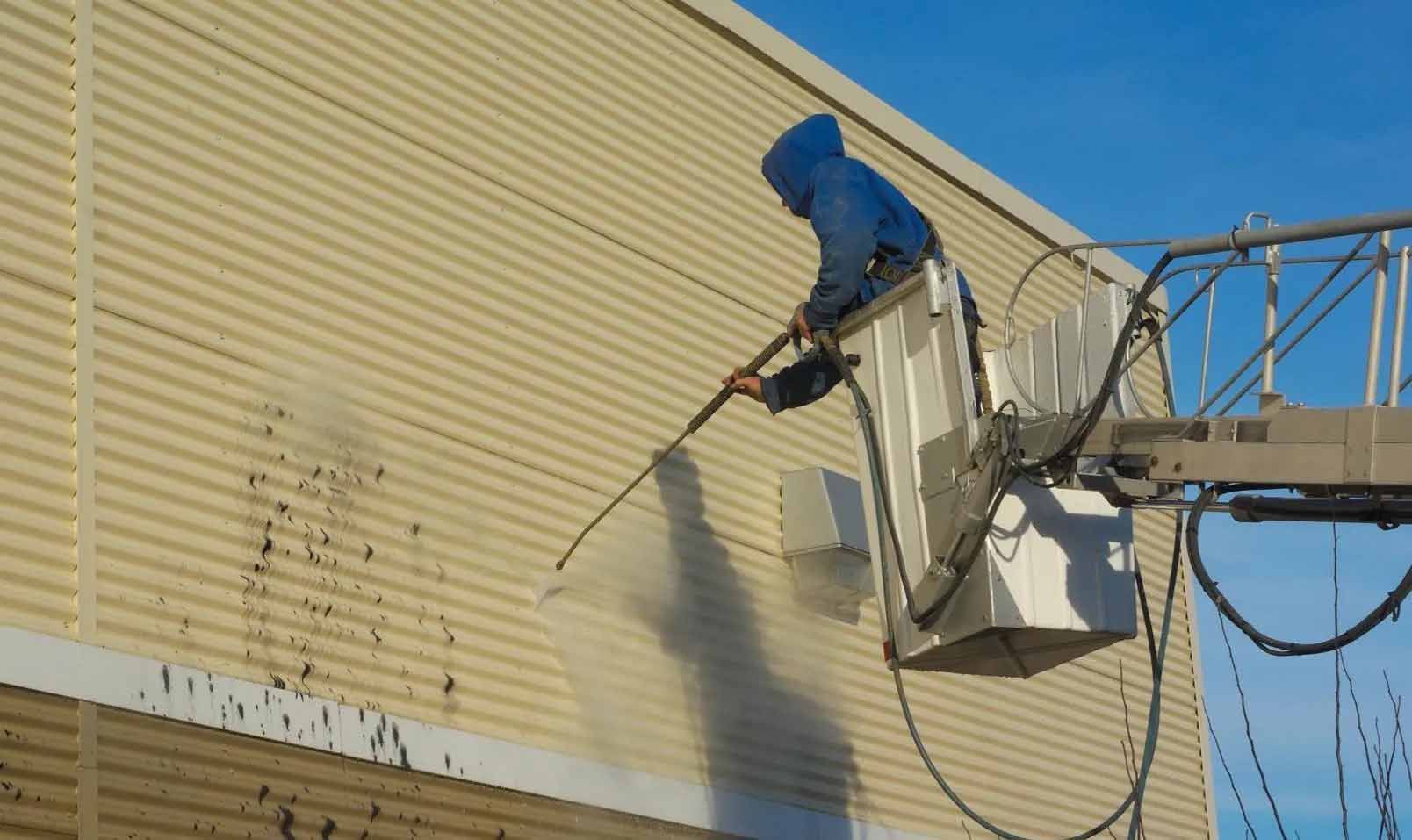 Un homme nettoie le côté d'un bâtiment avec un nettoyeur haute pression.