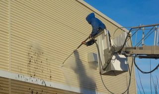 Un homme nettoie le côté d'un bâtiment avec un nettoyeur haute pression.